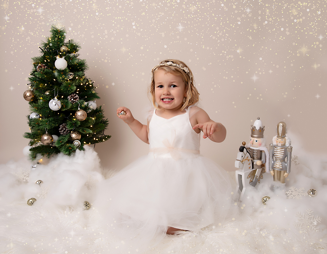 Young girl at her Christmas photoshoot playing with a jingle bell and smiling 