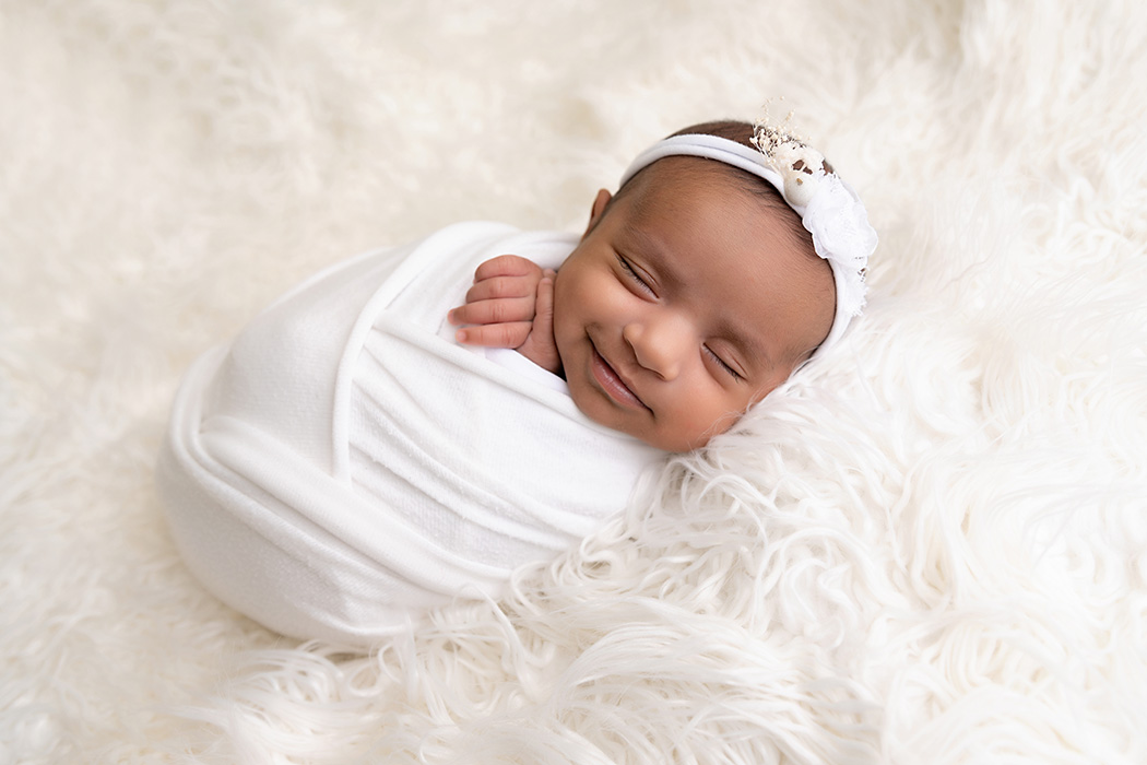6 week old newborn baby girl wrapped in white and smiling